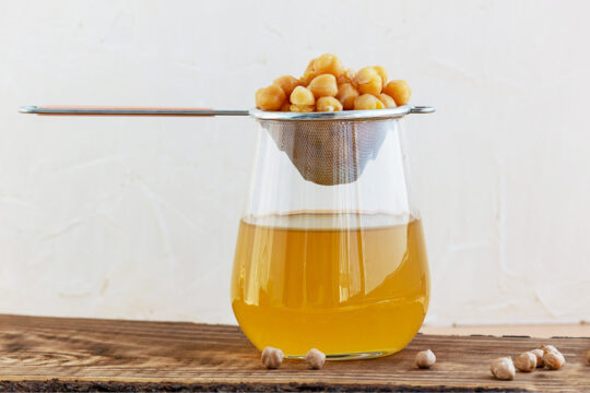 Zu sehen ist ein Glas mit aus Kicherebsen abgeseihten Wassers.