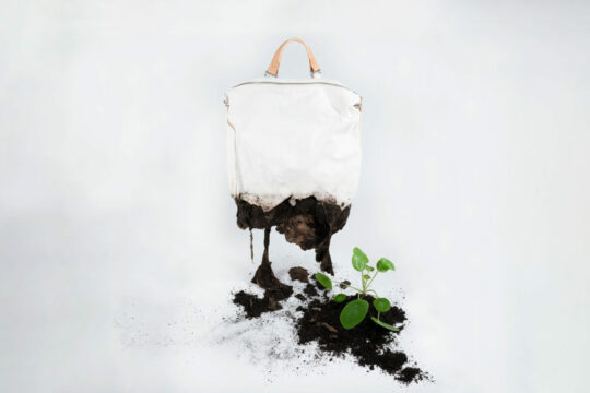 Man sieht einen Rucksack der sich unten zu Erde auflöst.