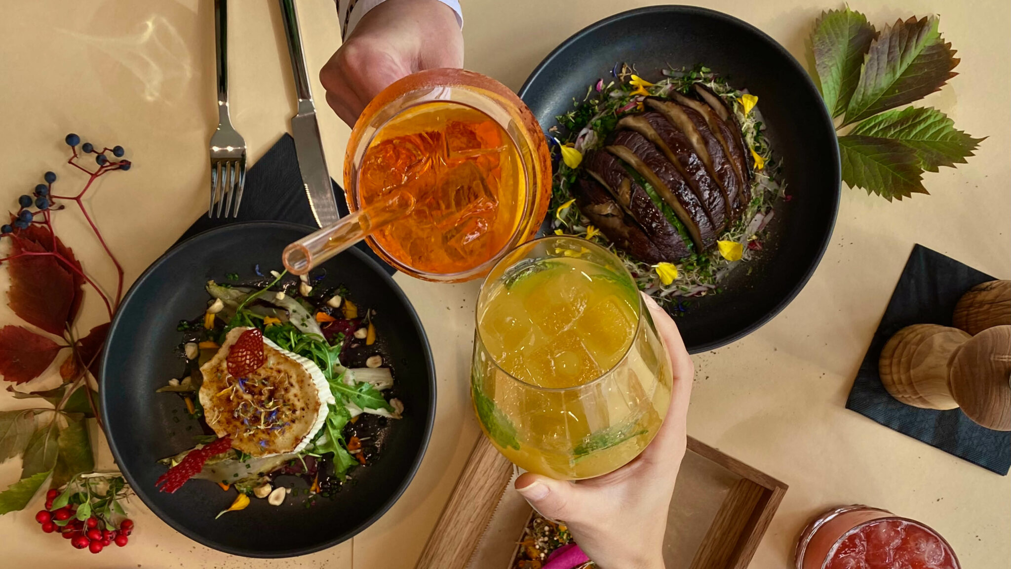 Man sieht einen gedeckten Tisch von oben, über dem die Hände von zwei Personen mit Getränken anstoßen.