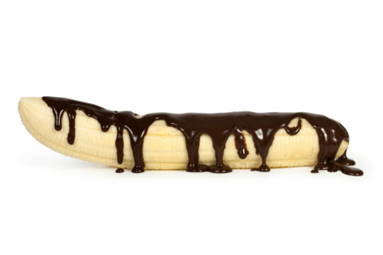Man sieht eine Banane, welche mit Schokosauce garniert ist.