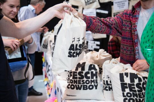 Man sieht wie auf einem Kleidermarkt gefüllte Jutebeutel übergeben werden.