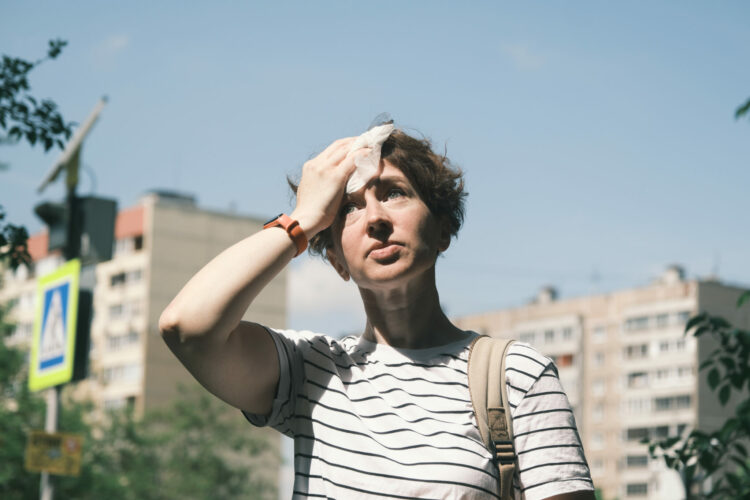 Eine Person in der Stadt wischt sich den Schweiß vom Kopf.