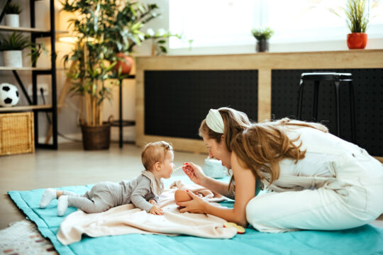 Ein Baby wird am Boden von einer Frau gefüttert.