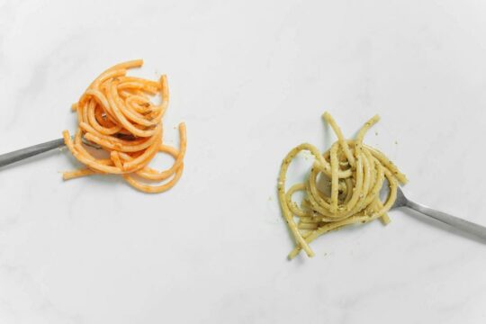 Zwei Gabeln mit Spaghetti in verschiedenfarbigen Saucen.