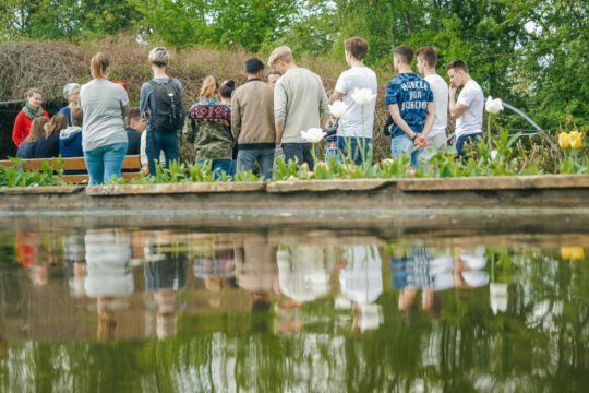 SchülerInnen die mit dem Rücken zu einem Teich stehen.