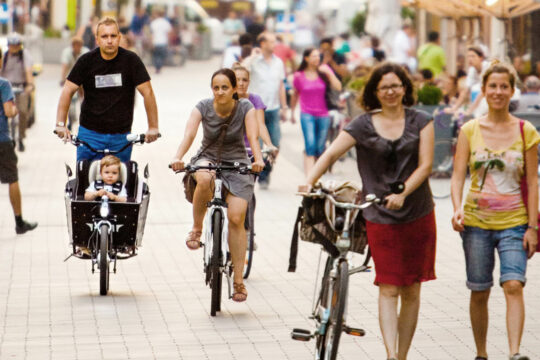 Personen in einer Begegnungszone, teils zu Fuß, teils am Fahrrad unterwegs.