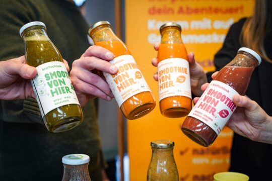 Vier Smoothies in Flaschen werden von Personen gehalten.