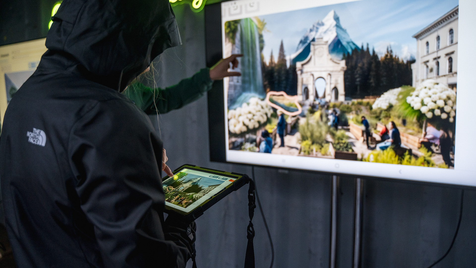 Eine Person steht mit einem Tablet vor einem Screen.