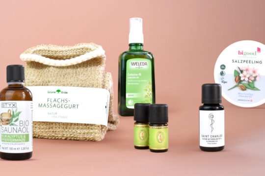 Mehrere Produkte, die für die Sauna oder die Pflege danach genutzt werden können vor einem altrosa Hintergrund.