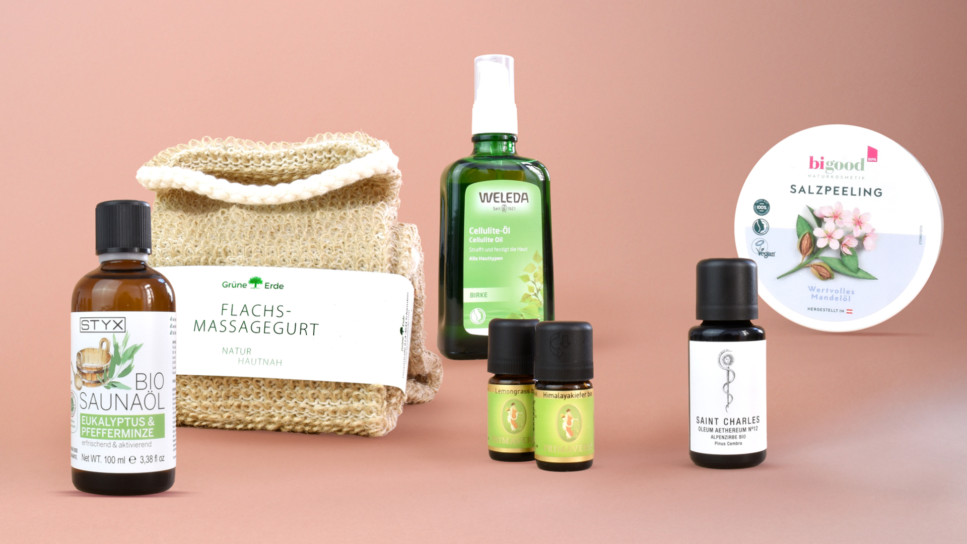 Mehrere Produkte, die für die Sauna oder die Pflege danach genutzt werden können vor einem altrosa Hintergrund.