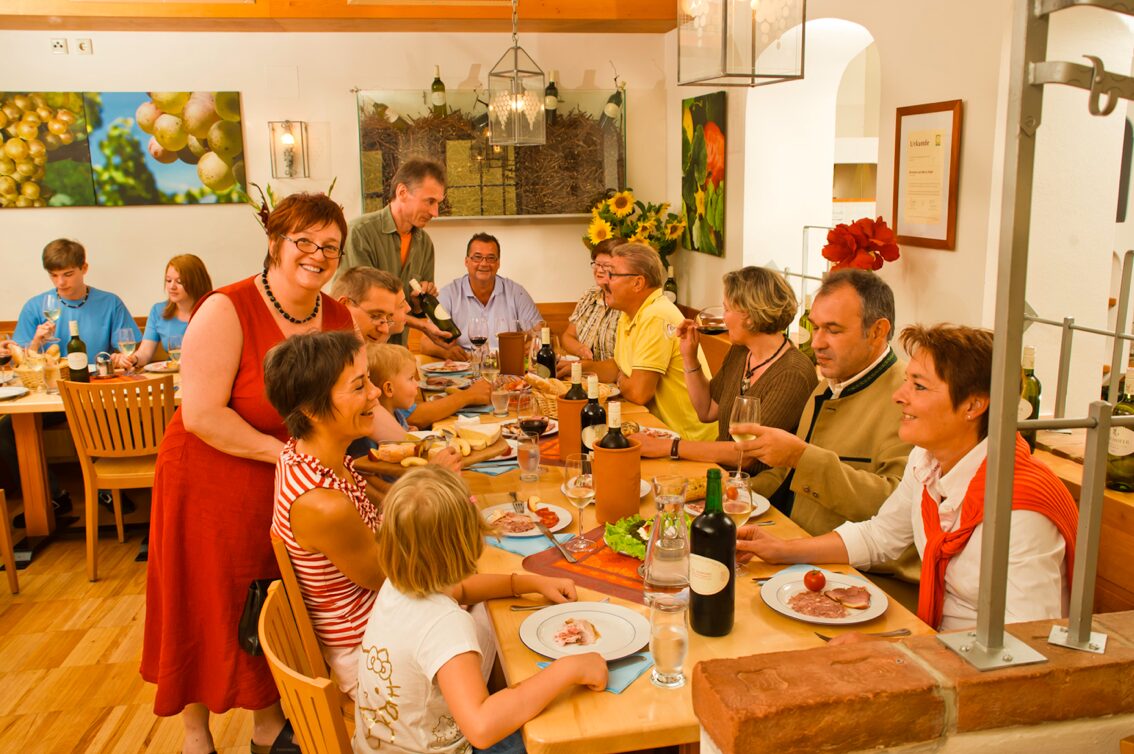 Mehrere Menschen sitzen an einem Holztisch, ihnen wird Essen serviert.