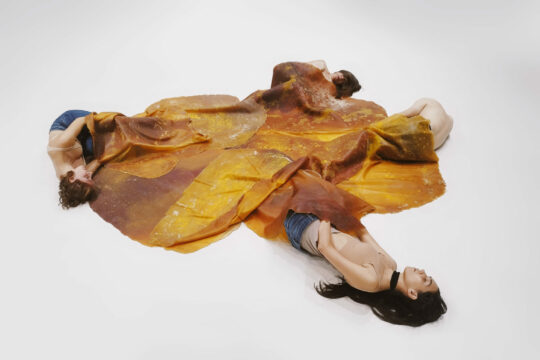 Mehrere Personen liegen auf einem weißen Untergrund und sind mit einer Art Decke zugedeckt.