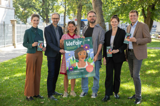 Mehrere Personen präsentieren ein Plakat für eine Messe.