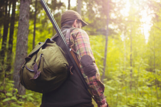 Ein Mensch geht mit einem Jagdgewehr durch den Wald.