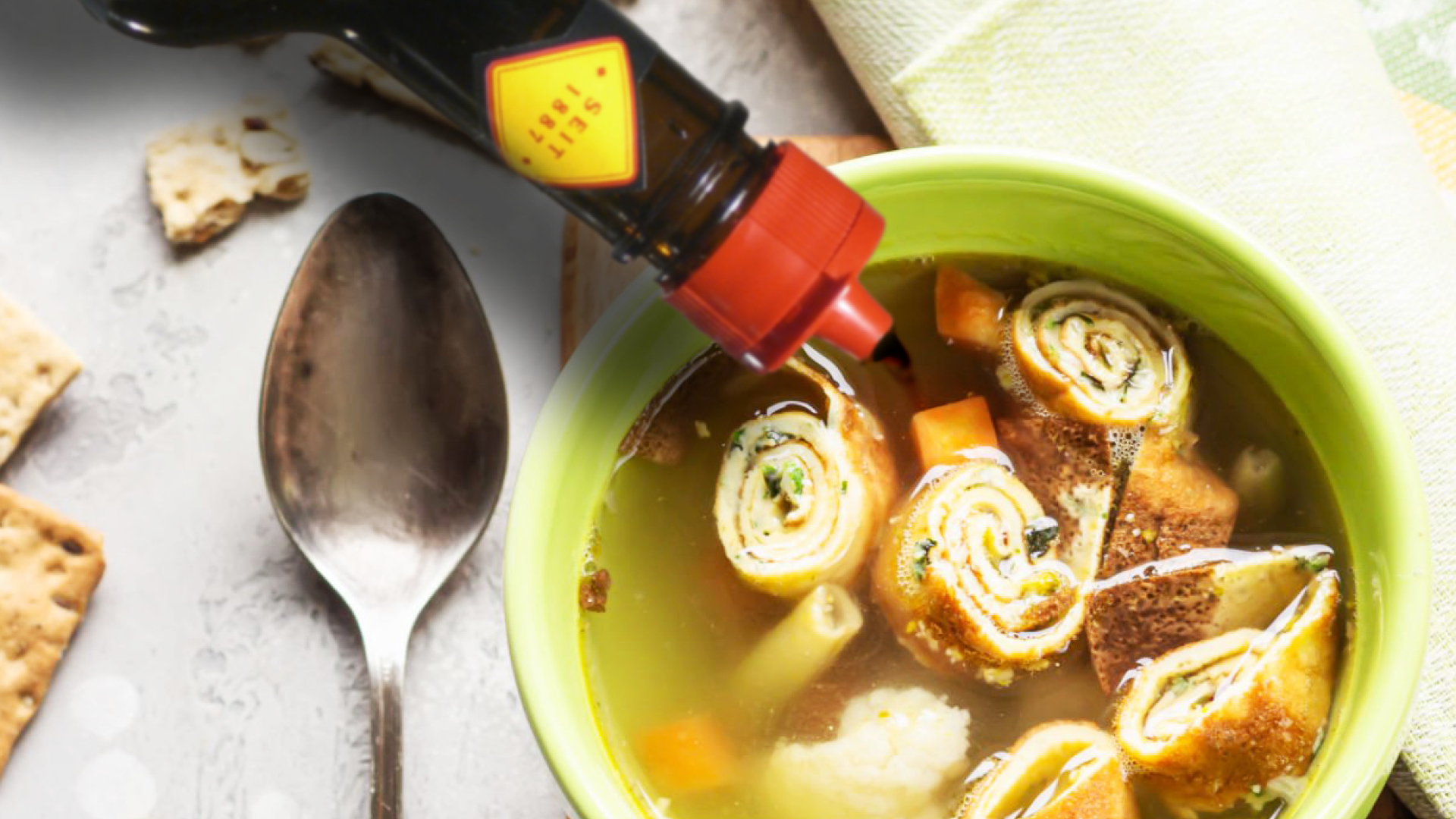 In eine Suppenschüssel fließt eine Gewürzsauce aus einer Glasflasche mit rotem Deckel.