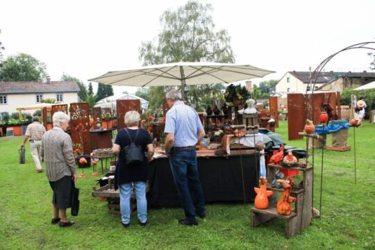 Mehrere Personen stehen an einem Stand auf einer Messe und betrachten Pflanzen.