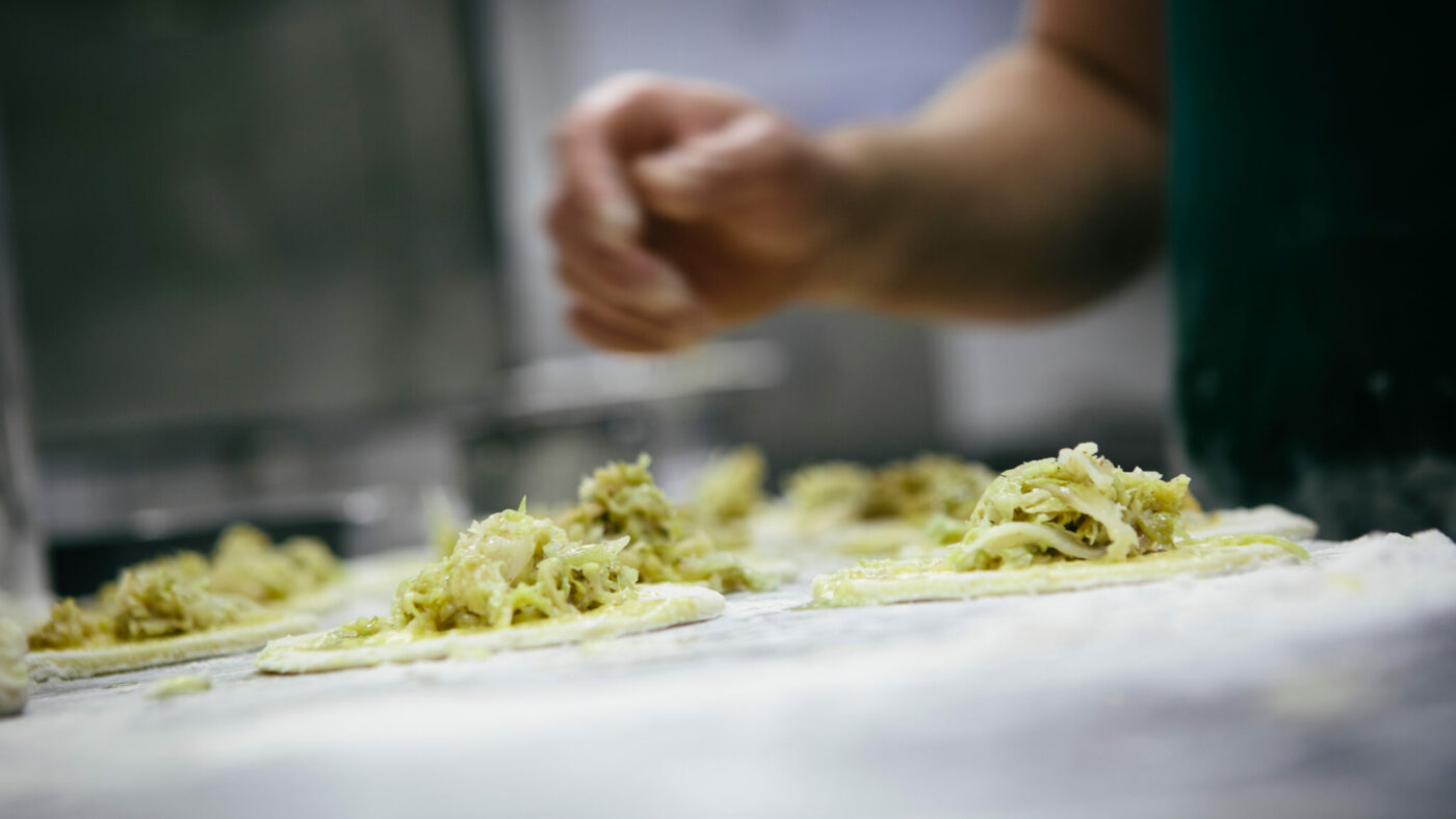Zu sehen sind mehrere Gerichte in der Zubereitung, dahinter die Hand einer Person.