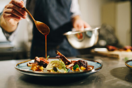 Eine Person fügt Sauce von einem Löffel auf ein Gericht hinzu.