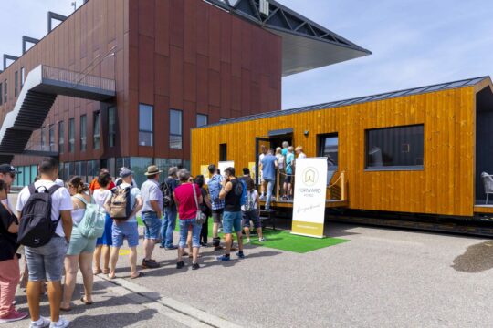 Mehrere Menschen stehen auf einer Messe vor einem kleinen Gebäude.