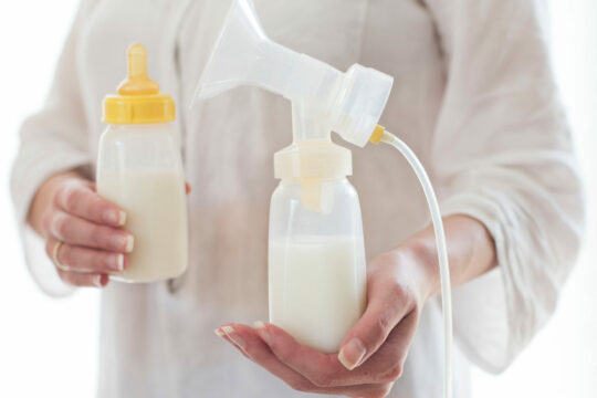 Eine Person in weißer Kleidung hält eine Pumpe und eine Flasche mit weißem Inhalt.