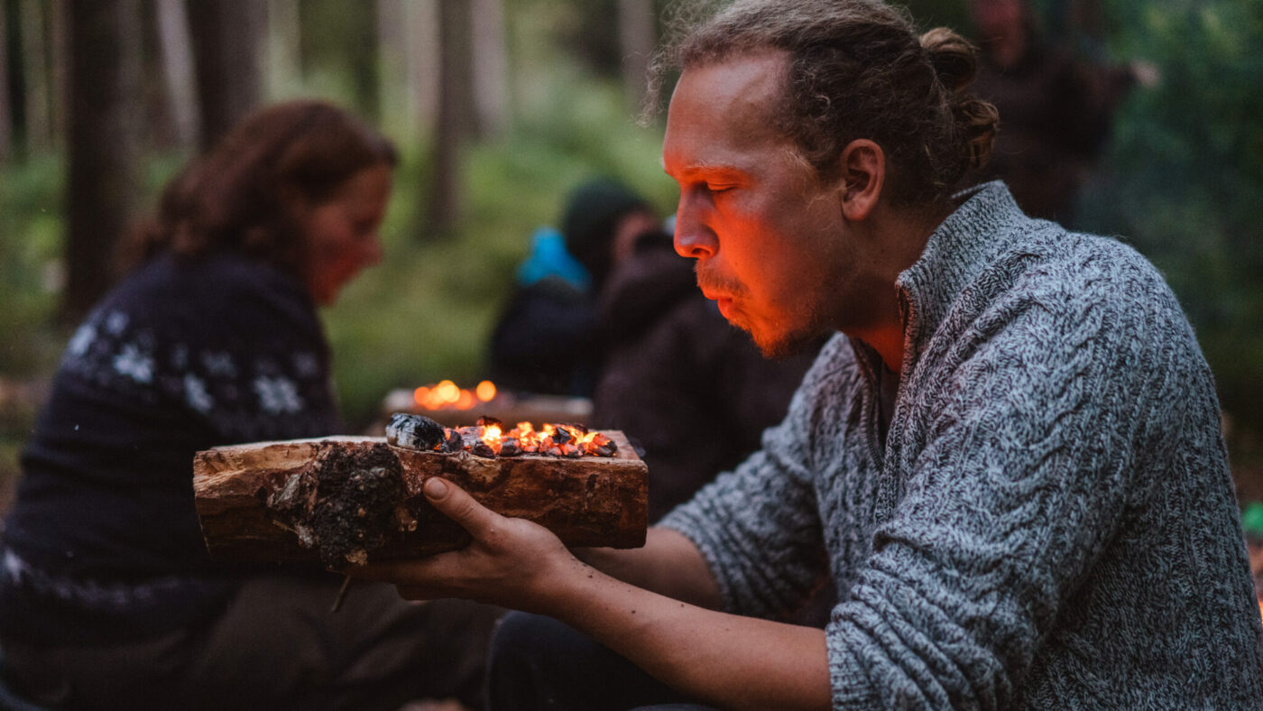 Eine Person bläst auf leicht brennendes Holz.