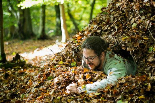 Eine Person schaut aus einem großen Laubhaufen heraus und lächelt.