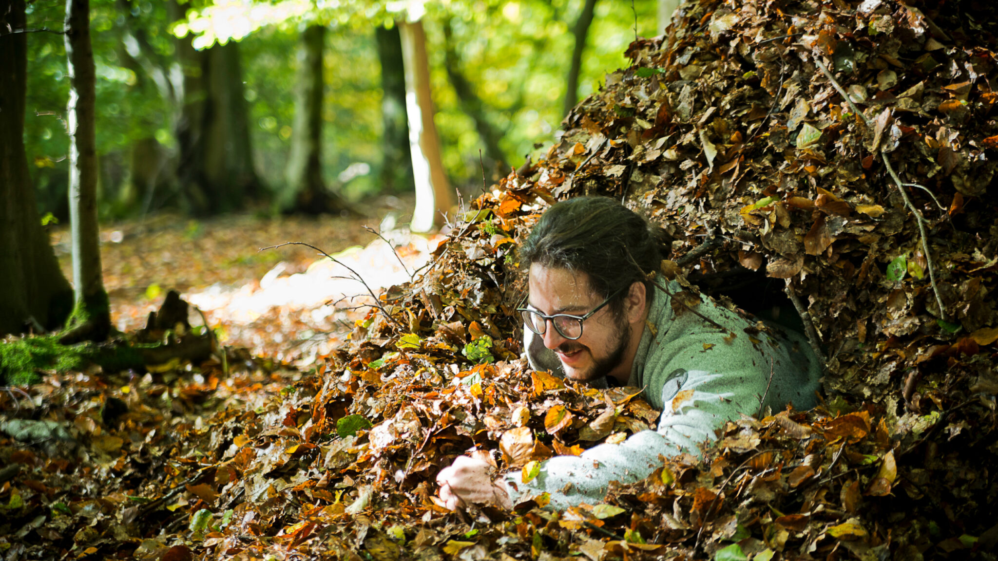 Eine Person schaut aus einem großen Laubhaufen heraus und lächelt.