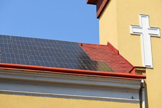 Ein Dach auf dem Photovoltaik-Panele und daneben ein Kreuz zu sehen sind.