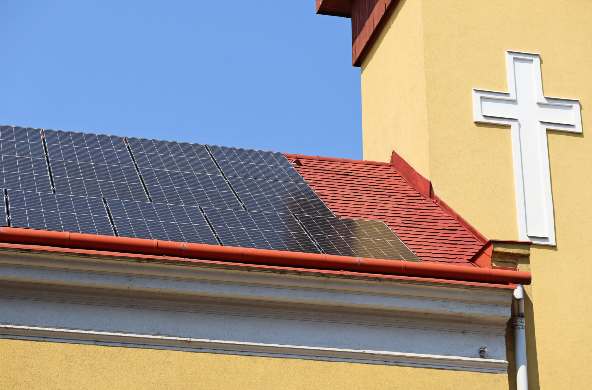 Ein Dach auf dem Photovoltaik-Panele und daneben ein Kreuz zu sehen sind.