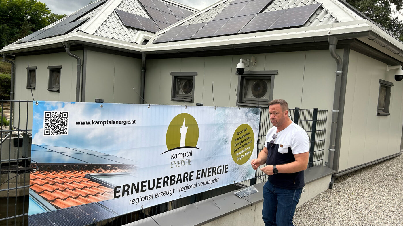 Eine Person trägt einen Banner vor ein Haus, auf dessen Dach sind PV-Zellen zu sehen.